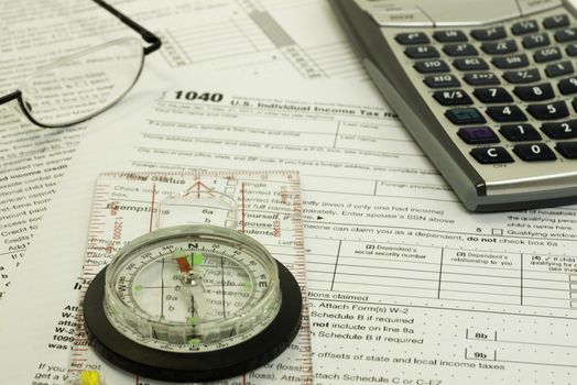 compass in focus with 1040 tax form, calculator, and glasses in background