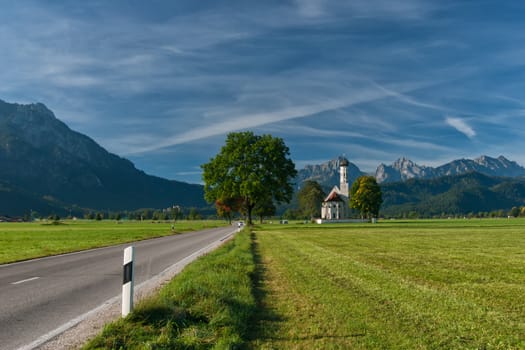 Autumn landscape with road, tree, church, mountains and sky on backgruond