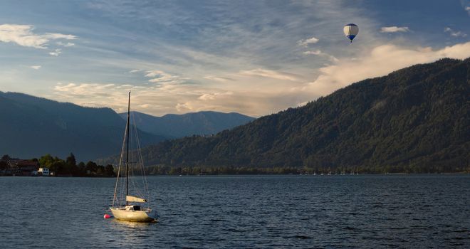 Morning on Lake Tegernsee, with yacht on water and air baloon in the sky, Alpes Pikes in the background, panorama