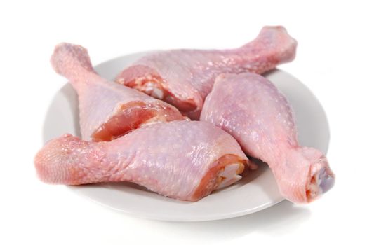 Four fresh raw chicken legs on plate isolated on white background