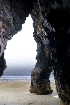 a rock formation from the cliffs onto the beach in ballybunion county kerry ireland with people swimming in background