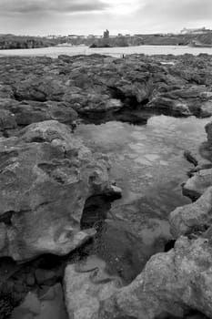 strange rock formations on the beach in ballybunion county kerry ireland with town and castle in background in black and white