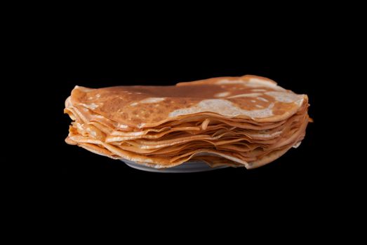 Russian pancakes pile on plate, isolated on black background