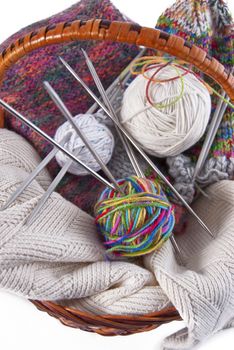 Balls of wool and knitting needles in basket on a white