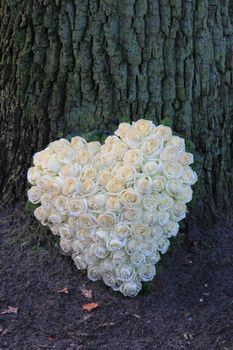 A sympathy flower arrangement near a tree in the shape on an heart