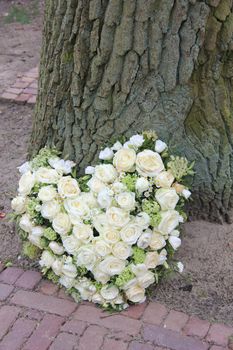 A sympathy flower arrangement near a tree in the shape on an heart