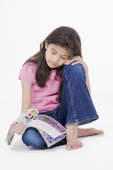 Ten year old Asian girl sitting on floor reading a magazine, isolated on white. All photos of flowers on magazine are those of the photographer herself. Use allowed.