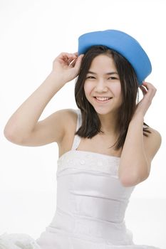 Beautiful young teen girl in blue hat and white dress, smiling. Isolated on white