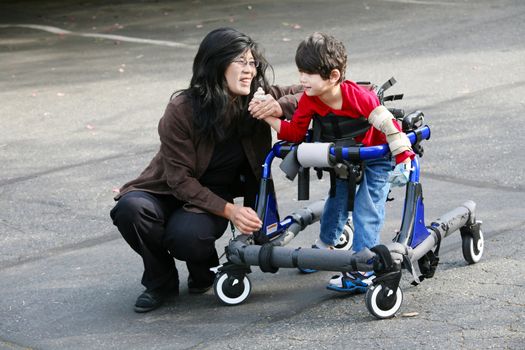 Mother with disabled son walking outdoors with walker, medical mobility equipment