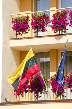 Lithuania and European Union flag hanging under building balcony with flowers.