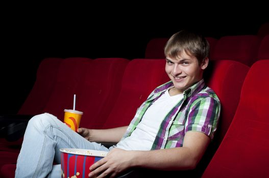 man in a movie theater, watching a movie and drink a drink