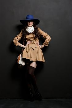 Expressive fashion studio shot of young and beautiful woman wearing brown overcoat on dark background. (Professional makeup and hair style).