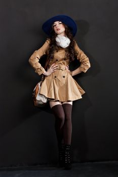 Expressive fashion studio shot of young and beautiful woman wearing brown overcoat on dark background. (Professional makeup and hair style).