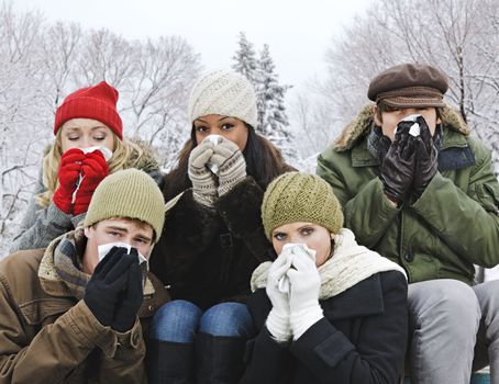Group of diverse young friends blowing noses outdoors in winter