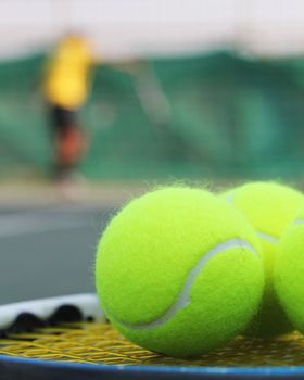 Tennis balls on racket strings with a sports person practising in the background