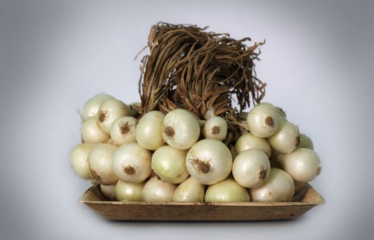 Bunch of white onions on a plate with dried leaves intact