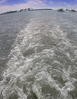 Wake or trail from a boat in arabian sea with fishing boats and shore visible in the backdrop. Photo taken near Udupi, Karnataka, India