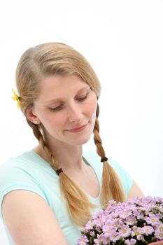 Portrait of blond female who is looking at pink flowers on white background