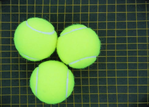Three tennis balls placed on a racket strings in the background