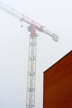 Red bwall made out of brick with construction crane in background in the fog