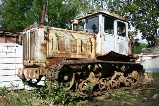 Tractor old in village at a fence from a white brick