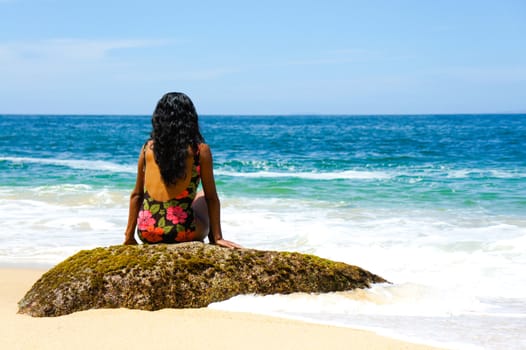 Latin woman sitting on a rock looking at the ocean in Puerto Vallarta, Mexico