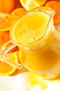 A glass of orange juice with oranges around it and a refrshing splash