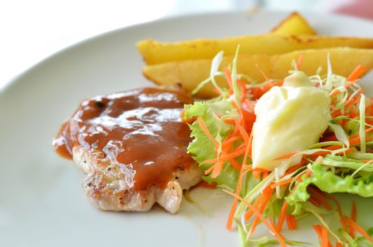 Grilled pork steak served with  tomato sauce, potatoes and vegetables ,