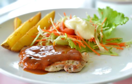 Grilled pork steak served with  tomato sauce, potatoes and vegetables ,