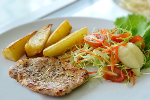 Grilled pork steak served with chips, potatoes and vegetables