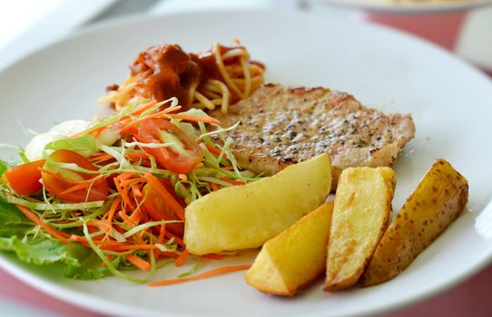 Grilled pork steak served with chips, potatoes and vegetables , macaroni