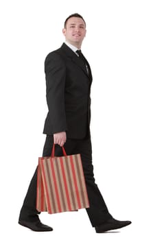 Young businessman with shopping bag walking against a white background.