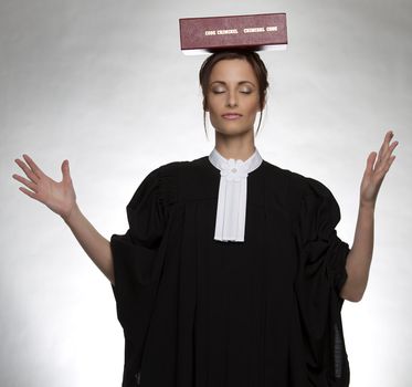 Women dress as a canadian attorney, with her eyes close, balancing a red book of criminal law with bilingual text on it on her head