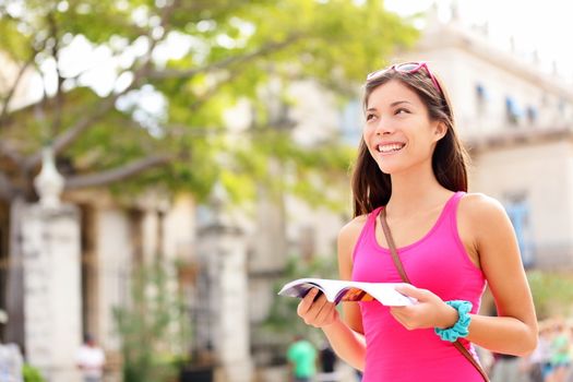 Tourist happy reading guide book. Woman traveler looking at copy space. Young female on vacation in Plaza de Armas, Old Havana, Habana, Cuba. Mixed race Asian / Caucasian young woman.