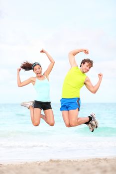 Fitness couple jumping fun on beach during outdoor workout running. Fit young Asian woman fitness model and Caucasian man.
