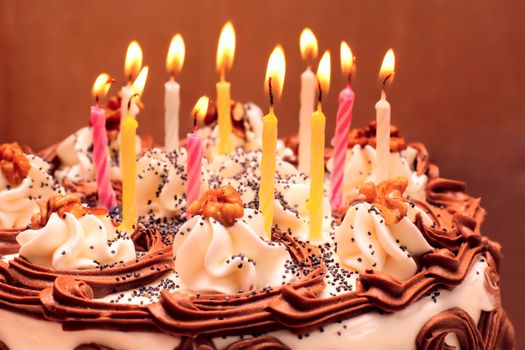 Birthday cake, lit candles on brown background
