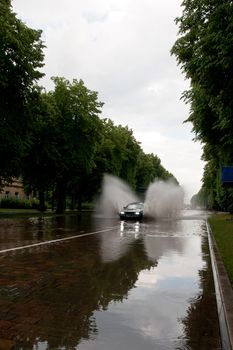after rain flooded city street and car splashes through
