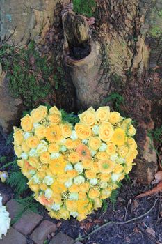 A sympathy flower arrangement near a tree in the shape on an heart