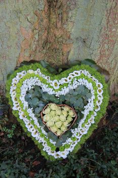 A sympathy flower arrangement near a tree in the shape on an heart