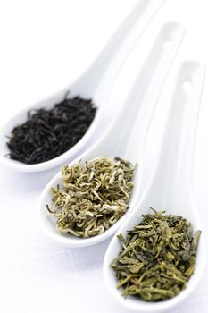 Black, white and green dry tea leaves in spoons