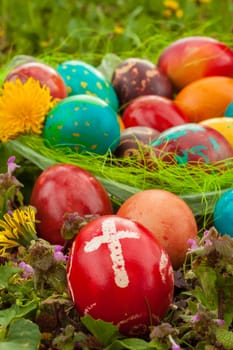 Colorful easter eggs with flowers, outside. Red egg with a cross on the front, vertical shot.