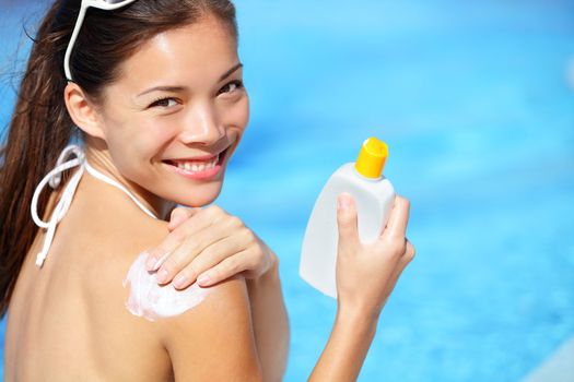 Sunscreen / sunblock. Woman putting solar cream on shoulder smiling happy outdoors by pool under sunshine on beautiful summer day. Mixed race Asian / Caucasian girl.
