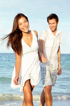 Beach couple happy holding hands. Young beautiful couple in love walking on beach at sunset. Asian woman, Caucasian man.