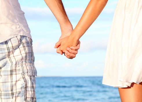 Holding hands couple on beach. Romantic love and happiness concept image with happy young couple. Closeup.