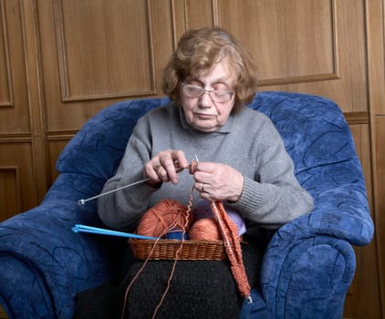 The old woman sits in an armchair and knits