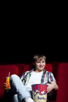 man in a movie theater, watching a movie and drink a drink