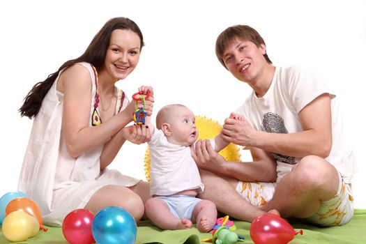 The young family, mum, the father and the son sit on a green plaid and play multi-colored balls