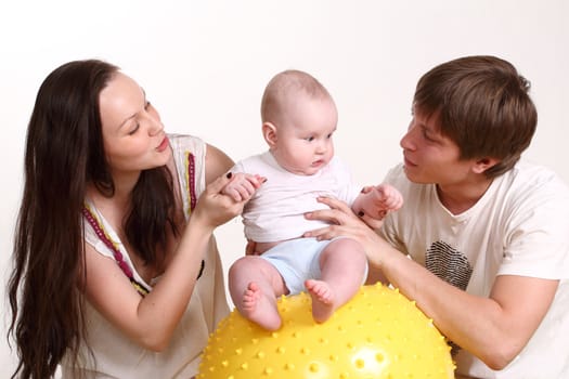 Portrait of a young family on a white background. The father, mum and the son. A horizontal format. The kid sits on a yellow ball, parents look at the kid