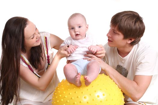 Portrait of a young family on a white background. The father, mum and the kid. A horizontal. The kid sits on a yellow ball, parents look at the kid