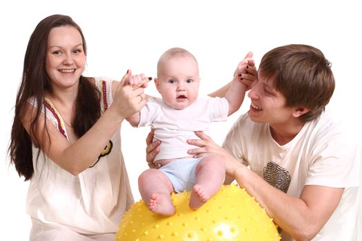 Portrait of a young family on a white background. The father, mum and the kid. A horizontal format. The kid sits on a yellow ball, parents hold it for hands.